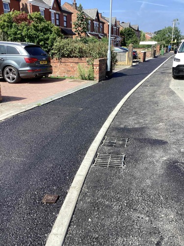 A photo of a finished, freshly tarmaced pavement in front of houses.